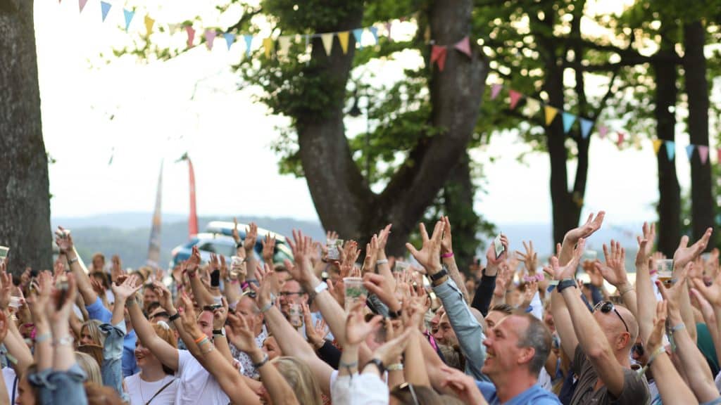 Mennesker som danser på festival utendørs med vimpler i trærne