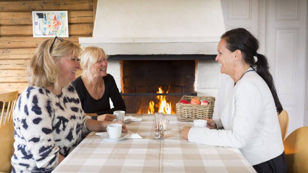 Tre damer snakker sammen ved en peis med fyr
