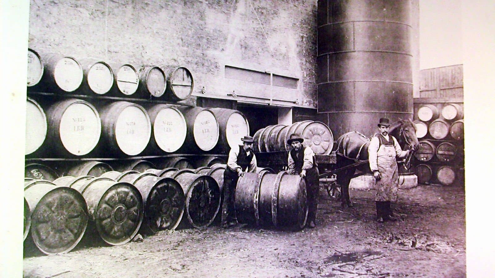 svarthvitt bilde av menn som ruller tønner med drikke