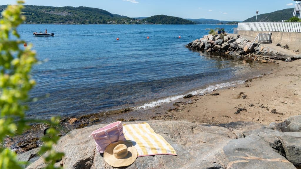 Strandhåndkle og solhatt på et svaberg ved en strand en sommerdag