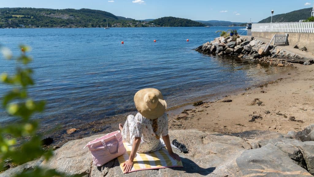 Lady in a hat sitting on a beach towel looking out over the water