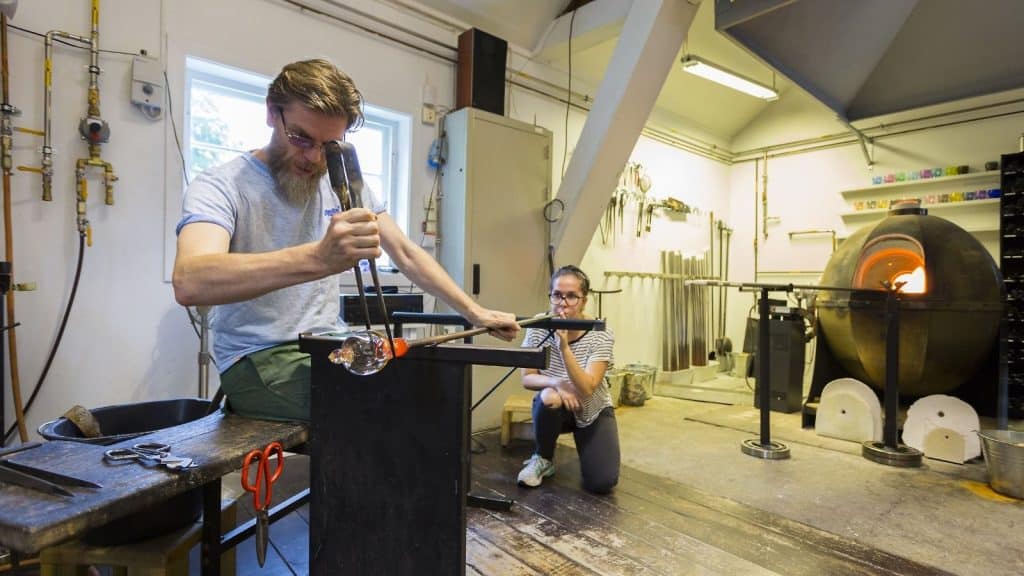En dame og en mann blåser glass inne i glasshytta på Bærums Verk
