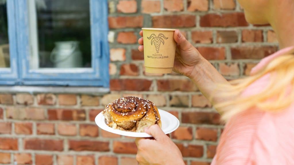 Dame som holder kaffe og kanelbolle utenfor et murhus