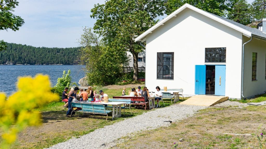 Besøkende som sitter på en uteservering ved fjorden med gul blomst i front