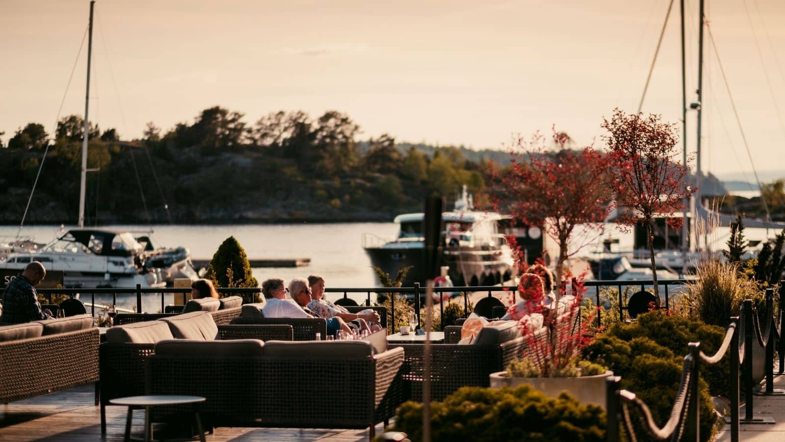 mennesker som sitter ute på en brygge i høstlige farger med Oslofjorden og båter bak