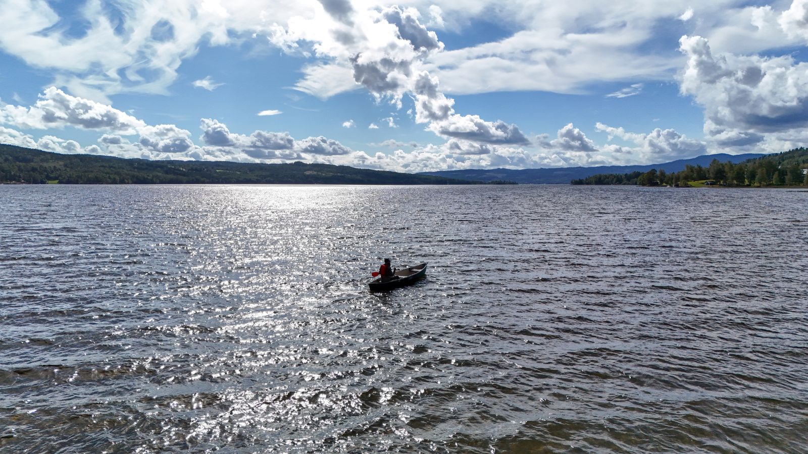person i båt på en innsjø omgitt av skog og fjelltopper