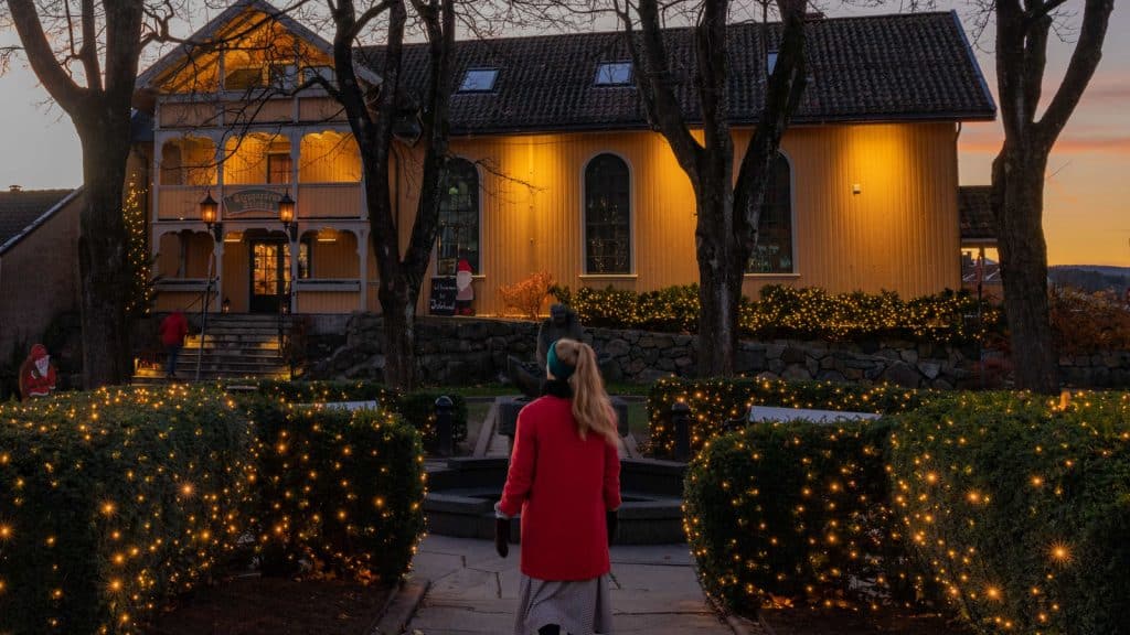 Dame som går utenfor et gult trehus i juletider