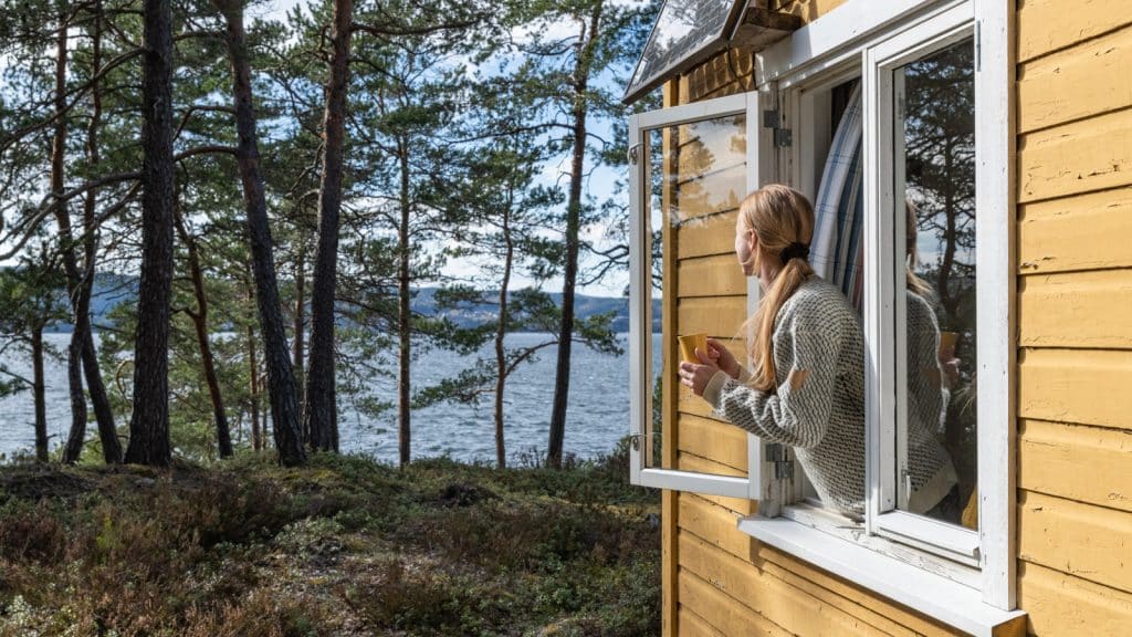 Lady looking out the window with a coffee cup at a yellow cabin