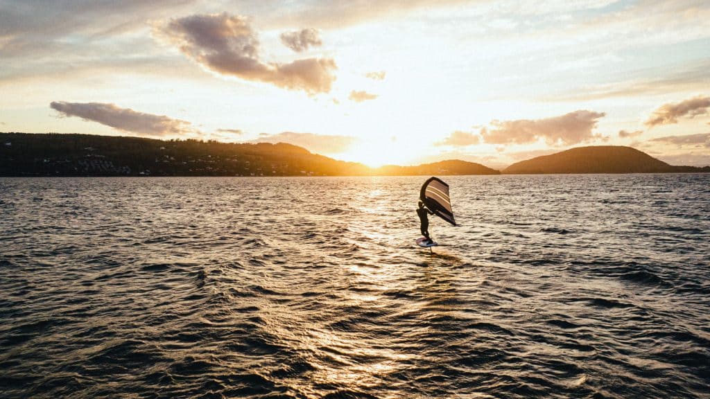 Mann som wingfoiler i fjorden i solnedgang