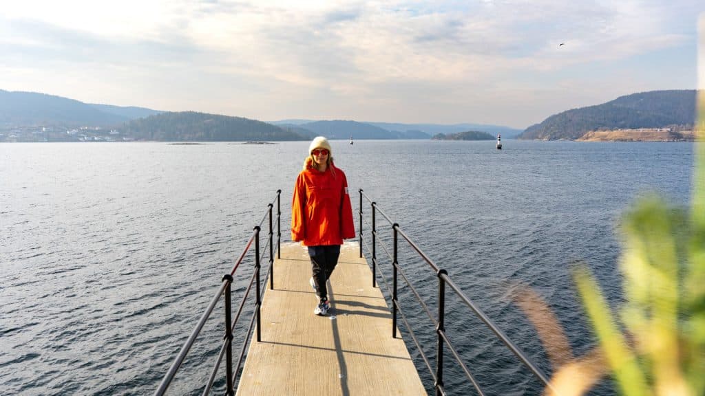 Dame i rød anorakk på et stupetårn ved en fjord