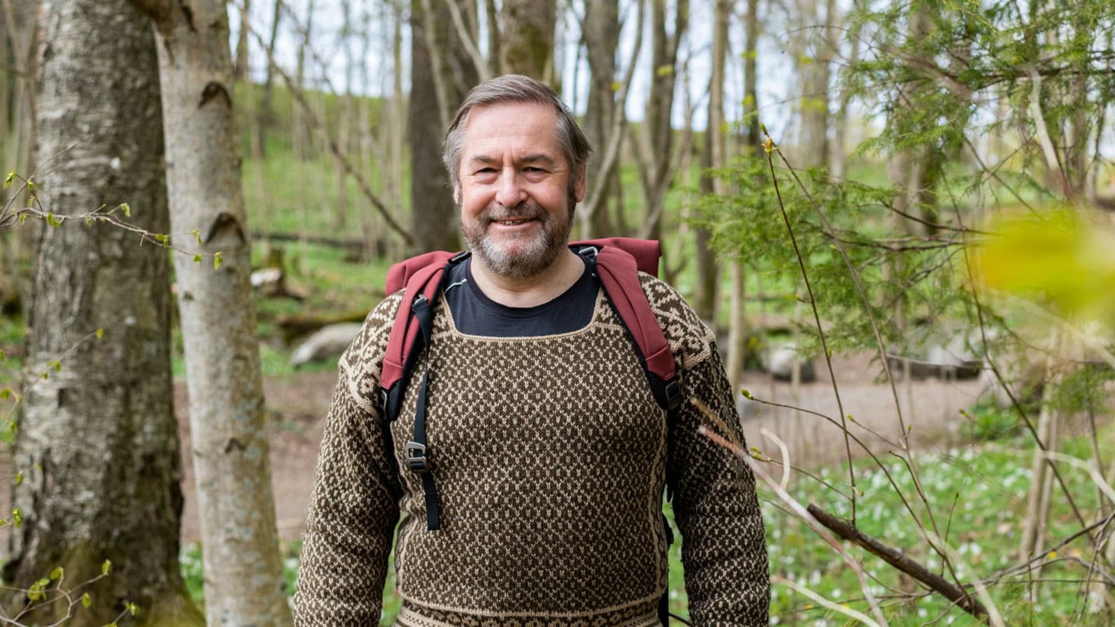 Mann som står med sekk og ullgenser i skogen